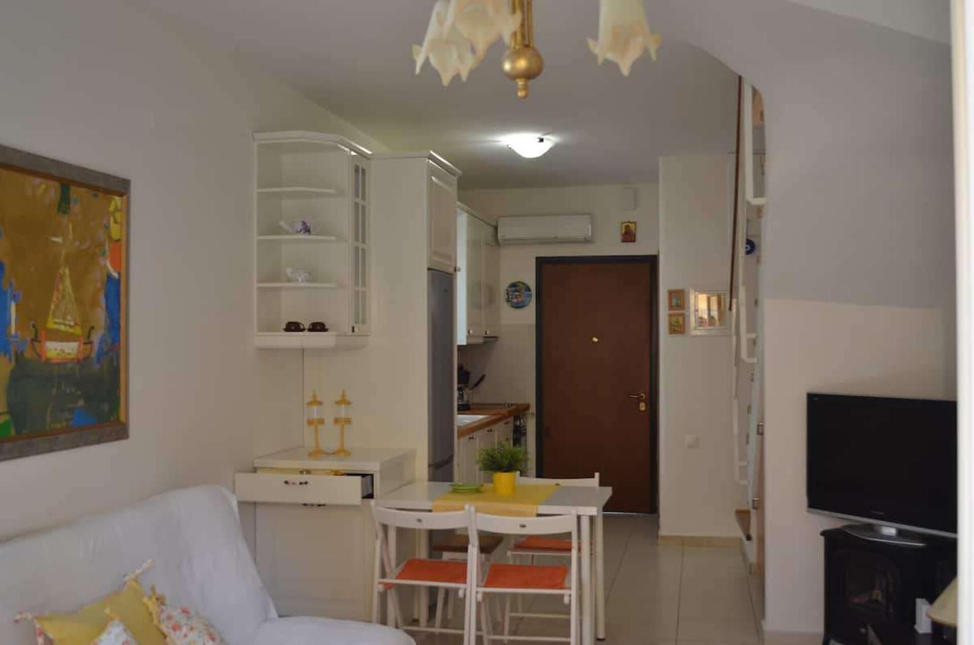 Una sala de estar con un sofá blanco, una mesa de comedor con sillas, un televisor y una zona de cocina con armarios y una puerta.