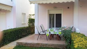 Een overdekte eethoek met een tafel en stoelen, een deur en een kleine tuin met gele bloemen.