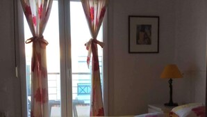 Een kamer met een bed, gordijnen, een lamp en een lijst met een foto aan de muur.