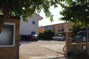 Ein Parkplatz mit befahrbarer Schranke, ein weißes Gebäude und ein Baum, der Schatten spendet.