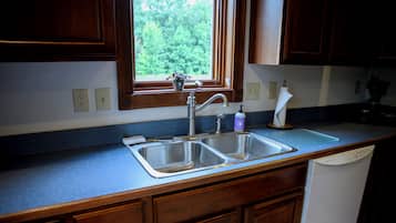 A kitchen with wooden cabinets, a double sink, a window with a view of greenery, and a dish soap bottle on the counter.