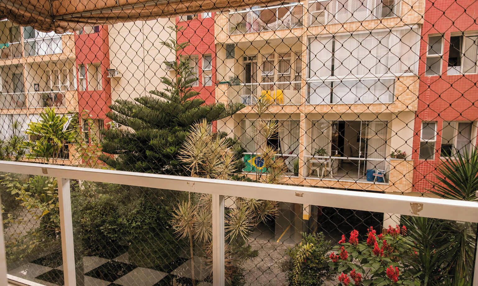 A multi-story residential building with balconies, surrounded by various plants and flowers.