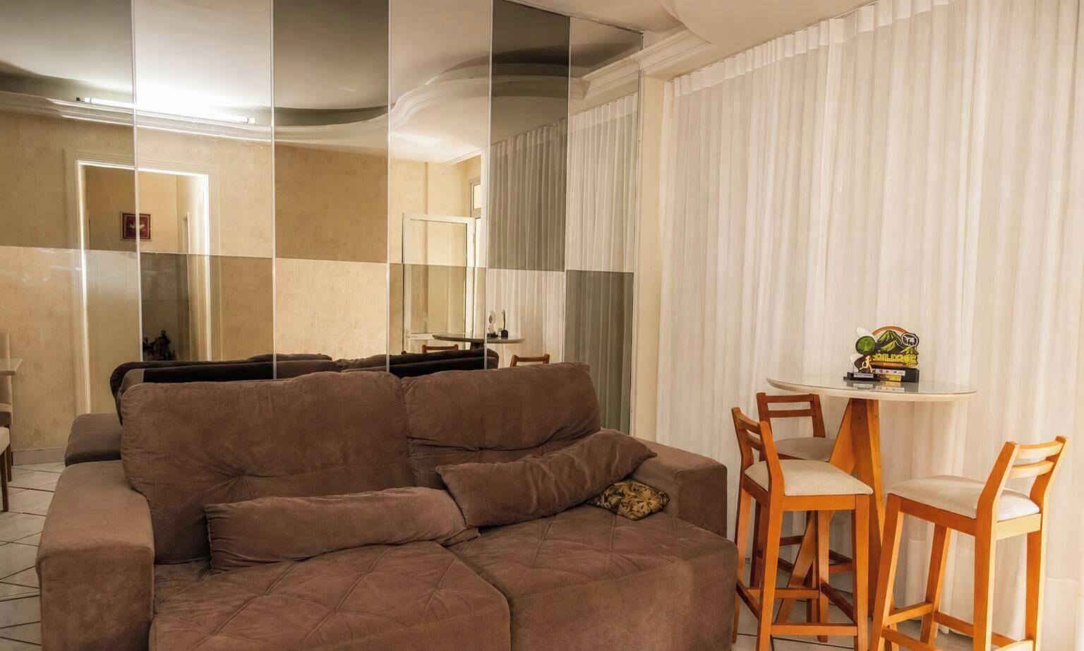 A living area with a brown sofa, a small round table with two chairs, and a mirror reflecting the room.
