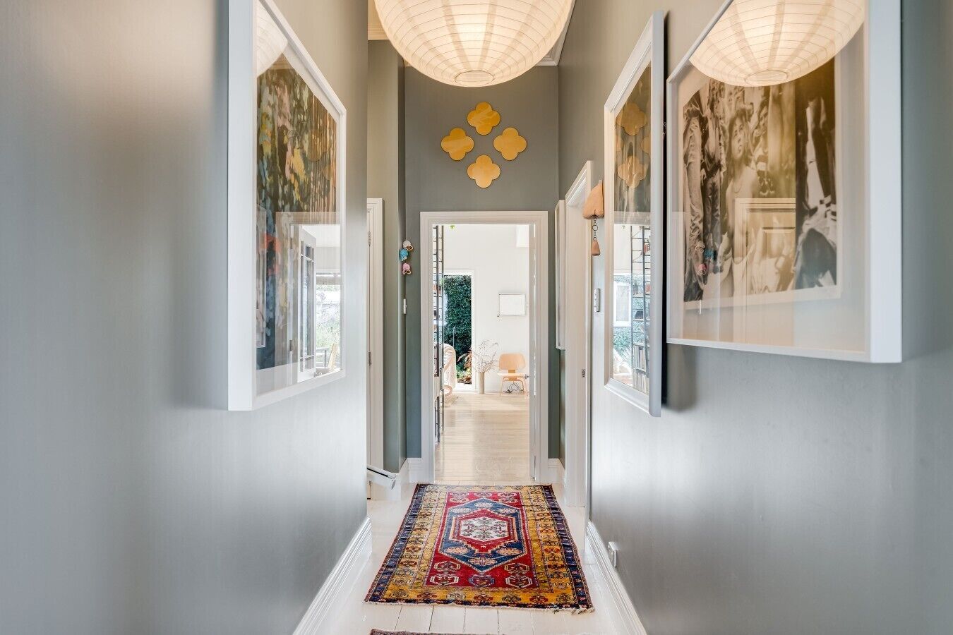 Un couloir orné d’un tapis à motifs, avec des œuvres d’art encadrées accrochées aux murs, et une porte donnant sur une autre pièce.