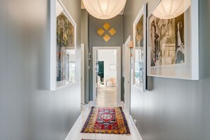 A hallway with a patterned rug, framed artwork on the walls, and a door leading to another room.