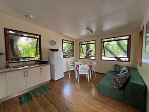 Eine kleine Küche mit einem Kühlschrank, einem Esstisch mit Stühlen und einem grünen Sofa mit Blumenkissen.