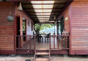 Eine Holzhütte mit einer Veranda, einem Essbereich mit Stühlen und einem Tisch sowie Blick aufs Meer.