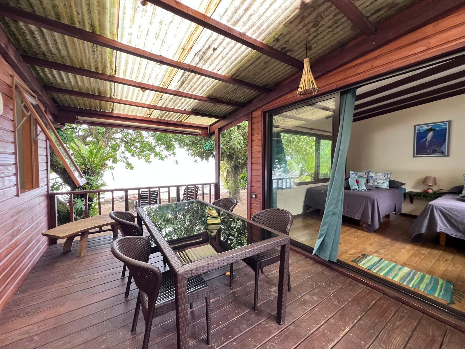A wooden deck with a glass door leading to a bedroom with a bed and a nightstand.