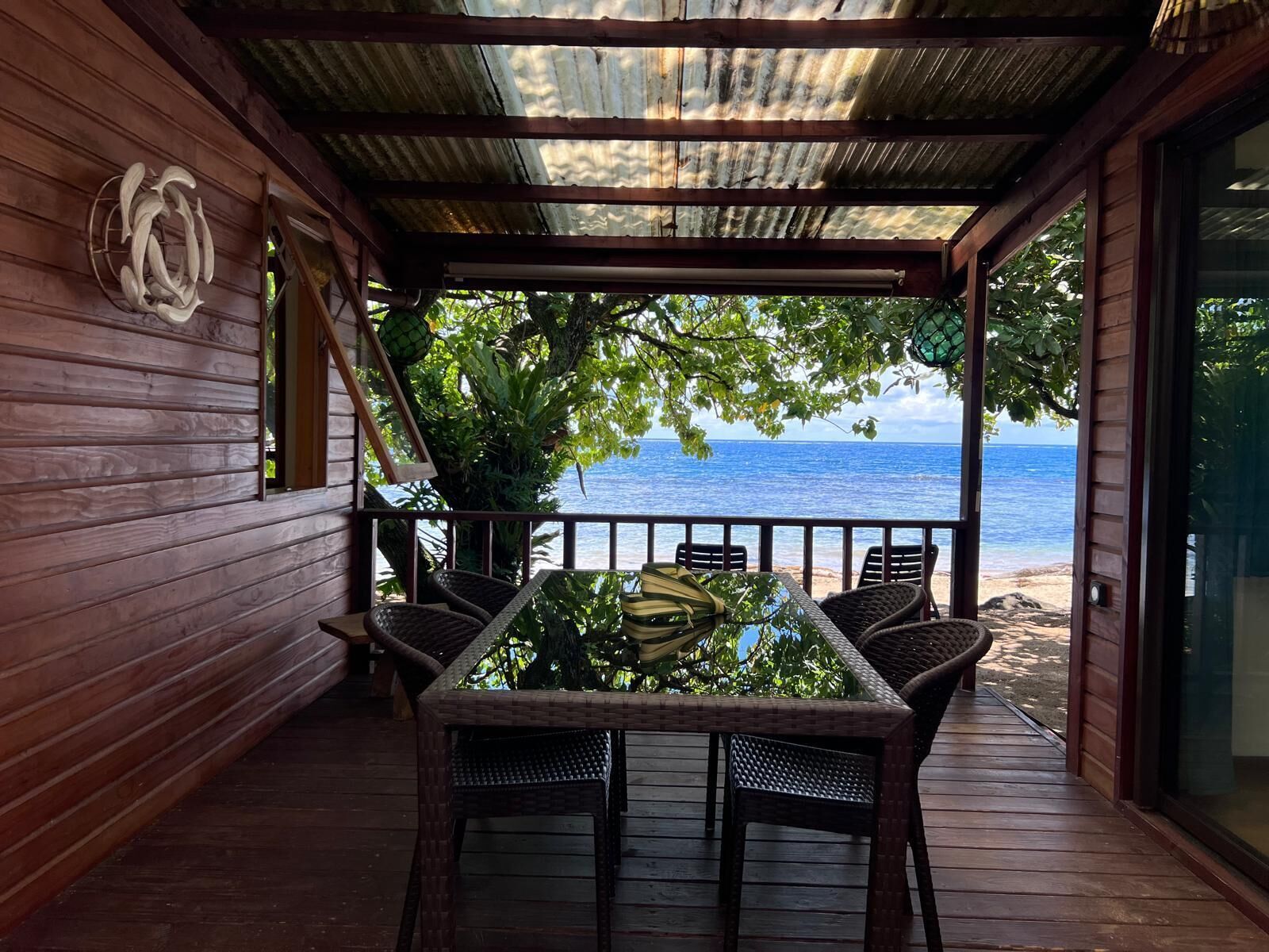 A covered outdoor seating area with a table and chairs, overlooking a beach.