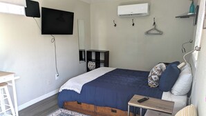 Een slaapkamer met een bed, een aan de muur bevestigde televisie, een airconditioningapparaat, een nachtkastje, een stoel en een hanglamp.