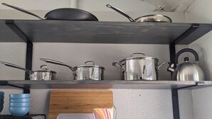 Een keukenkastje met pannen, een waterkoker en blauwe mokken.