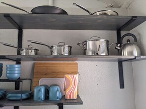 Une étagère de cuisine avec des ustensiles de cuisine, une bouilloire et des tasses bleues.