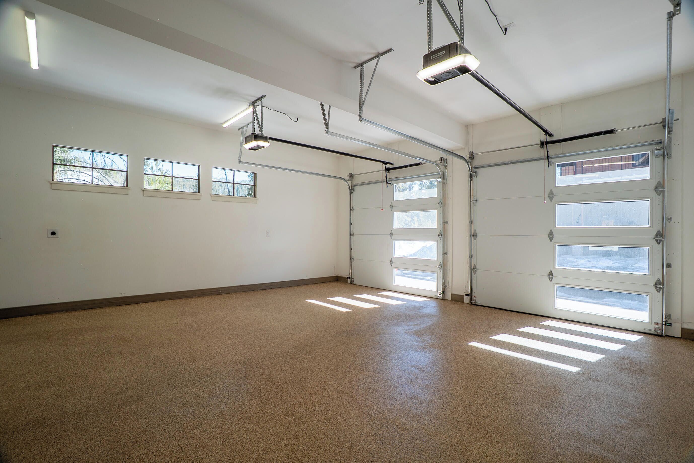 A spacious garage with a concrete floor, three windows, and a garage door.