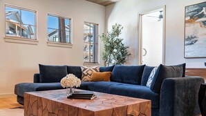 Ein modernes Wohnzimmer mit einem dunkelblauen Sofa, einem Holztisch und einem großen Fenster mit Blick auf ein Gebäude.