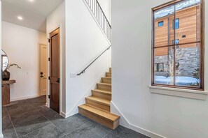 A modern interior with a staircase, a wooden door, and a window with a view of a building. - Peaceful Views | Hot Tub | Creekside Privacy (Winter Park)