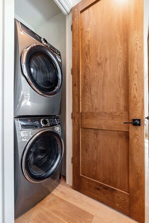A laundry room with a double-door washing machine and a wooden door. - Peaceful Views | Hot Tub | Creekside Privacy (Winter Park)
