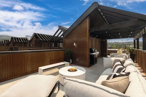 Eine Terrasse im Freien mit Grillbereich, Sitzgelegenheiten und Landschaftsblick.