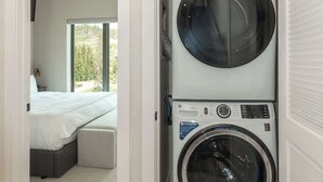 Ein Waschraum mit gestapelten Waschmaschinen und ein Bett im angrenzenden Schlafzimmer.