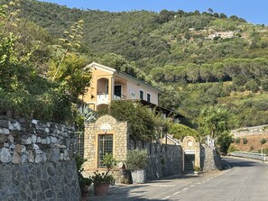 Ein Anwesen an einem Hang mit einer Steinmauer, ein gelbes Gebäude mit Balkon und eine gewundene Straße.