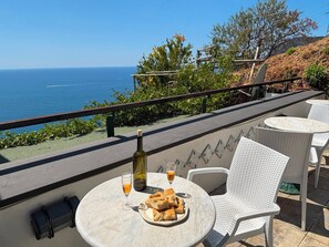 Eine Terrasse mit Tisch für zwei Personen, mit Blick aufs Meer, mit Flasche und Gläsern auf dem Tisch.