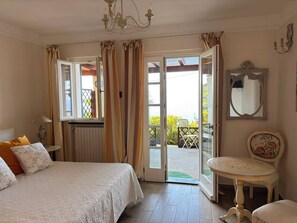 Ein Schlafzimmer mit Bett, Stuhl, Tisch, Spiegel und Blick ins Freie.