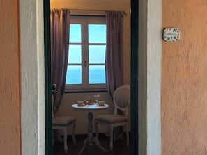 Um quarto com vista para o mar, uma mesa com um prato de comida e duas cadeiras.