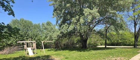 A park with a swing set, a paved path, and trees.
