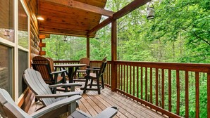 Une terrasse en bois, dotée de chaises Adirondack et d’une table, qui offre une vue sur une zone boisée.