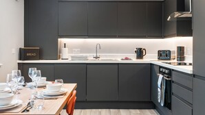 Una cocina moderna con armarios oscuros, una isla central y una zona de comedor preparada para cuatro.