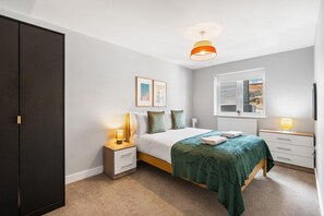 Ein Schlafzimmer mit Bett, Nachttischen, einem Kleiderschrank, einem Fenster mit Jalousien und einer Deckenleuchte.
