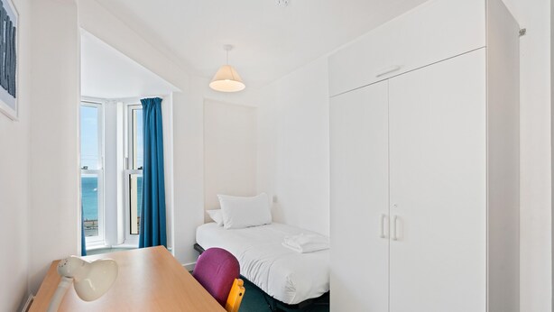 Ett hotellrum med en säng, ett skrivbord, en stol, en garderob och utsikt över havet.