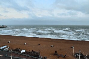 A beach with a pier in the distance, a sandy shore, and a building with a roof. - Kings Residence 7 | By My Getaways (Brighton)