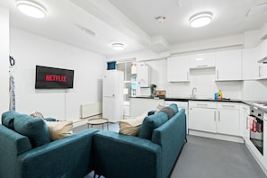 A modern kitchen with white cabinets, a built-in oven, and a sink. There is a flat-screen TV mounted on the wall with the word 'NETFLIX' displayed. - Kings Residence 7 | By My Getaways (Brighton)