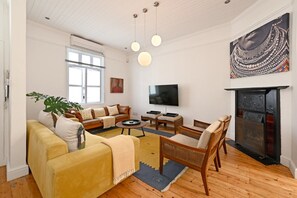 A living room with a sofa set, a coffee table, a television, a fireplace, and a large window. - Two Bed Home | Fresnaye | Secure | Spacious | BBQ (Cape Town)