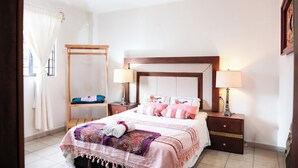 Ein Schlafzimmer mit einem Bett, zwei Nachttischen, einem kleinen Tisch, einem Holzstuhl und einem Fenster mit Vorhängen.