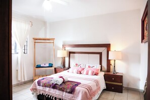A bedroom with a bed, two bedside tables, a nightstand, a wooden chair, and a window with curtains. - Bright apartment with a small pool, just 15 minutes from downtown Oaxaca. (Oaxaca de Juárez)