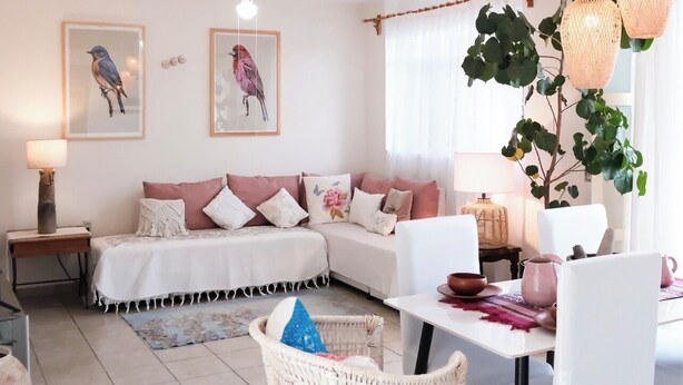 Ein modernes Wohnzimmer mit einer Couch, einem Esstisch, Stühlen, einer großen Pflanze und Kunstwerken an den Wänden.