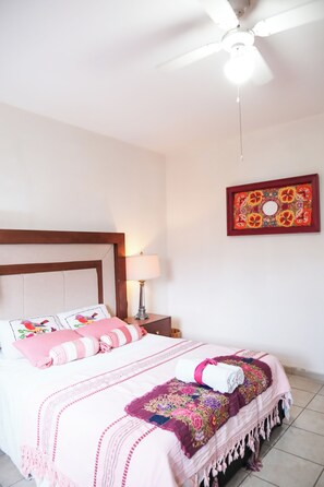 Hotelkamer met een bed, plafondventilator, nachtkastje met lamp en decoratieve wanddecoratie.