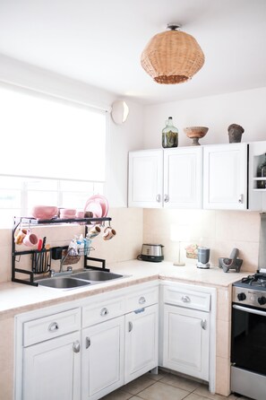 A kitchen with white cabinets, a sink, a stove, and a hanging light fixture. - Bright apartment with a small pool, just 15 minutes from downtown Oaxaca. (Oaxaca de Juárez)