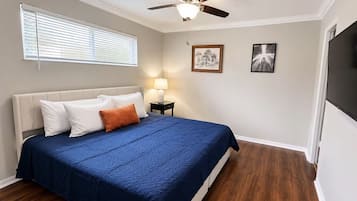A bedroom with a bed, a ceiling fan, a nightstand with a lamp, and two framed pictures on the wall.