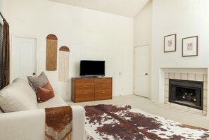 A living room with a sofa, a television on a wooden cabinet, a fireplace, and wall-mounted art. - Casa Vista  Designer Home Pool Sleeps 16 (San Antonio)