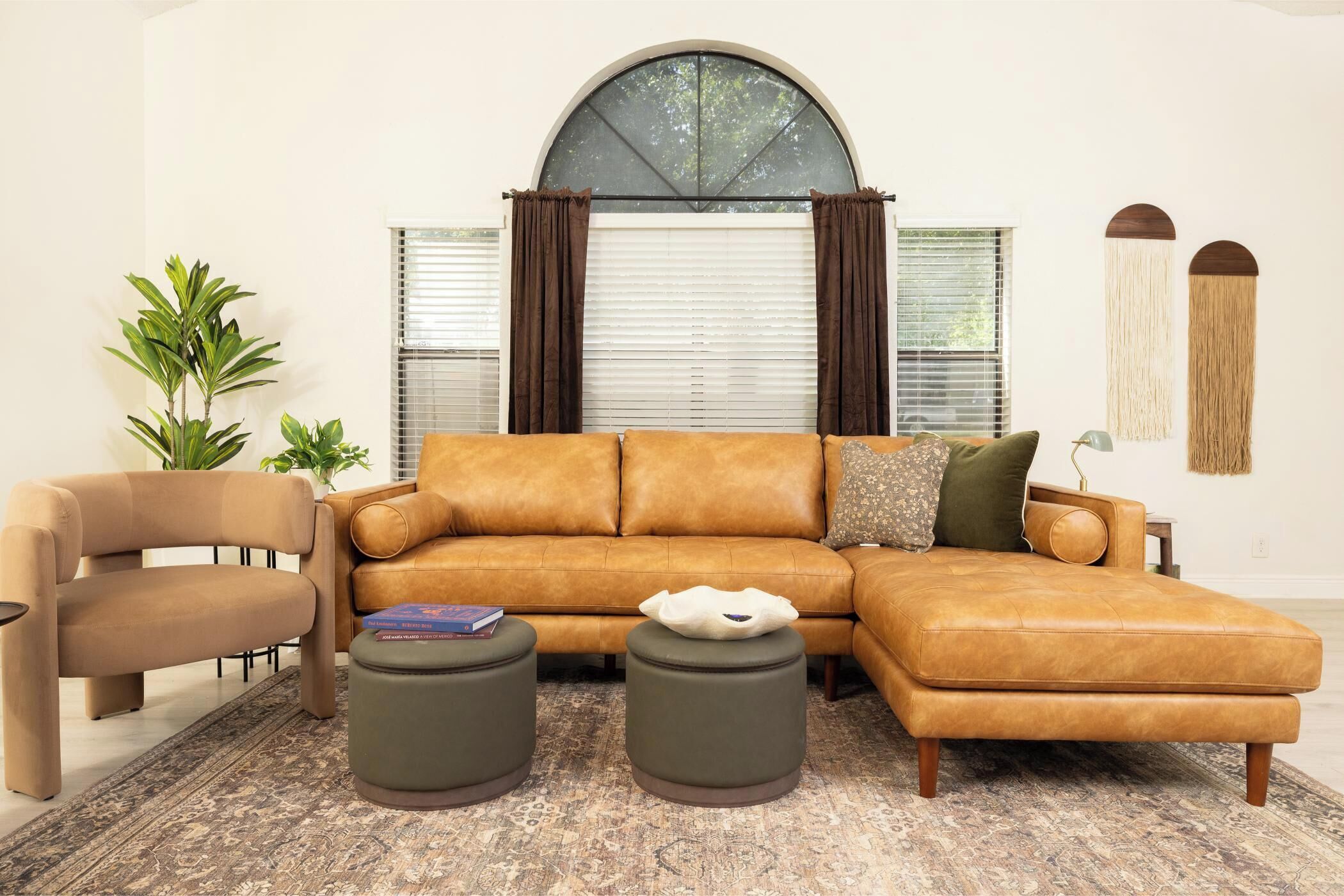 A living room with a sectional sofa, a chair, two ottomans, a rug, and a large window with curtains.