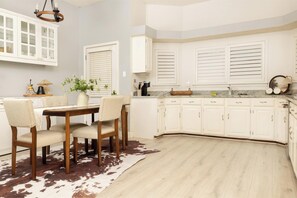A kitchen with white cabinetry, a dining table with chairs, and a cowhide rug. - Casa Vista  Designer Home Pool Sleeps 16 (San Antonio)