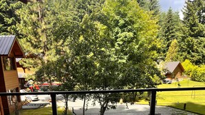 Una terraza de madera con una mesa lista para una comida, con vistas a una zona boscosa y una carretera con edificios.