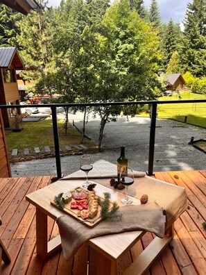Eine Holzterrasse mit gedecktem Tisch, mit Blick auf eine bewaldete Gegend, in der eine Straße und Gebäude sichtbar sind.