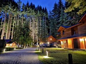 Eine Lodge mit Schotterauffahrt, umgeben von hohen Bäumen, und Holzhütten mit sichtbaren Fenstern und Türen.