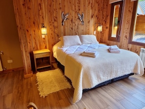 Quarto com painéis de madeira, uma cama, mesas de cabeceira e luzes fixadas na parede.