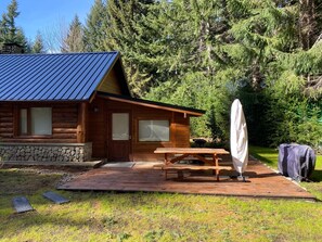 A wooden cabin with a stone foundation, a covered picnic table, and a large umbrella. - Cabañas en el bosque patagónico (Villa La Angostura)