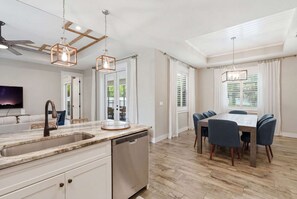 A modern kitchen with a built-in dishwasher, a dining area with a wooden table and chairs, and pendant lighting. - Kid-Friendly Bonita Home With Private Pool & Spa (Bonita Springs)