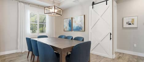A dining area with a wooden table and blue chairs, a chandelier, and a sliding barn-style door.